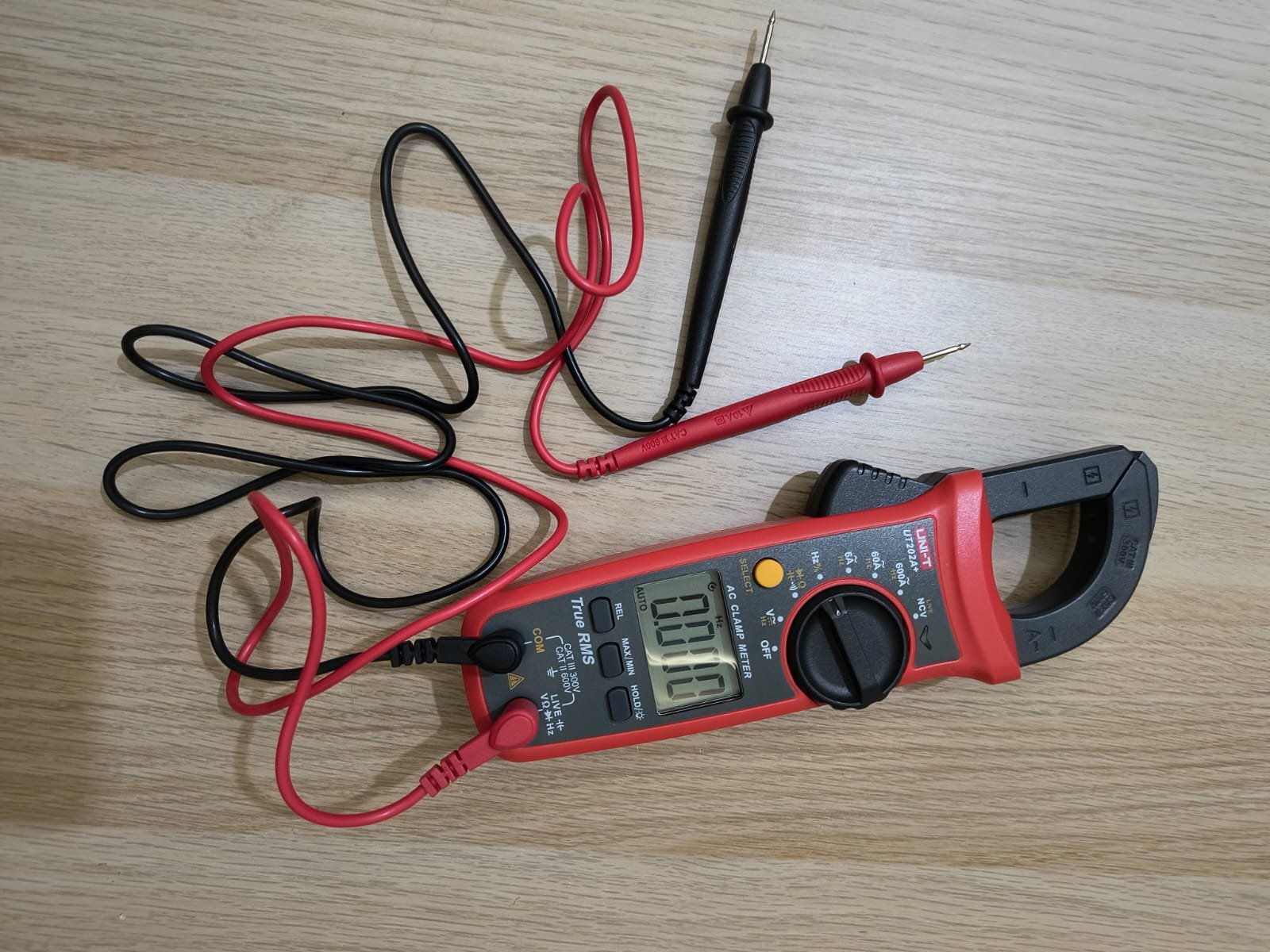A high-quality close-up photo of a professional UNI-T digital clamp meter with red and black testing probes on a wooden surface.
